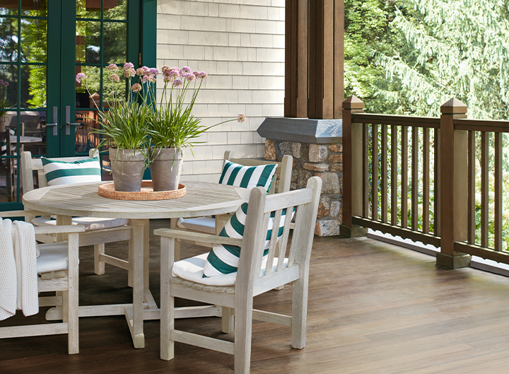 An outdoor living area featuring a wooden deck and ceiling, white brick walls with green trim, and a white table with matching chairs.